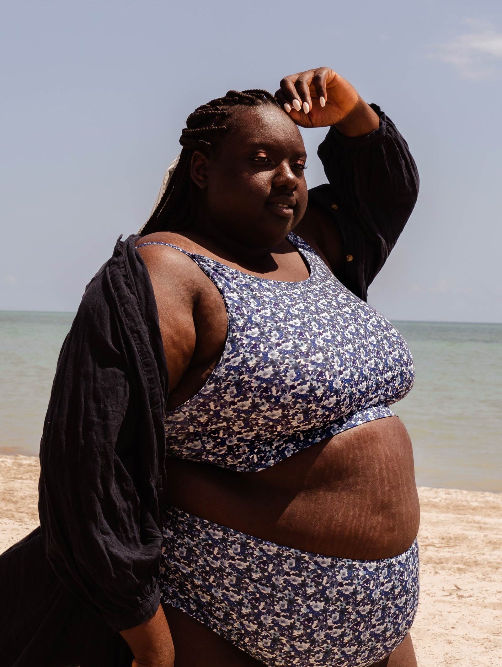 A plus-size woman standing on a beach with her Mango Moonflower Bralette Bikini Top