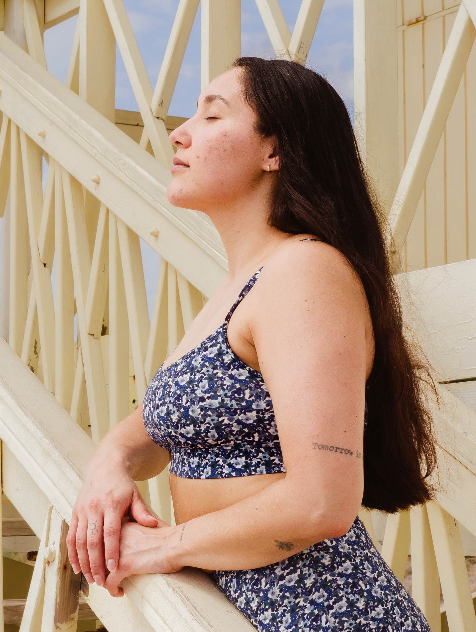 A woman leaning on a staircase with her eyes closed wearing the Mango Moonflower Bralette bikini top by mimi and august.