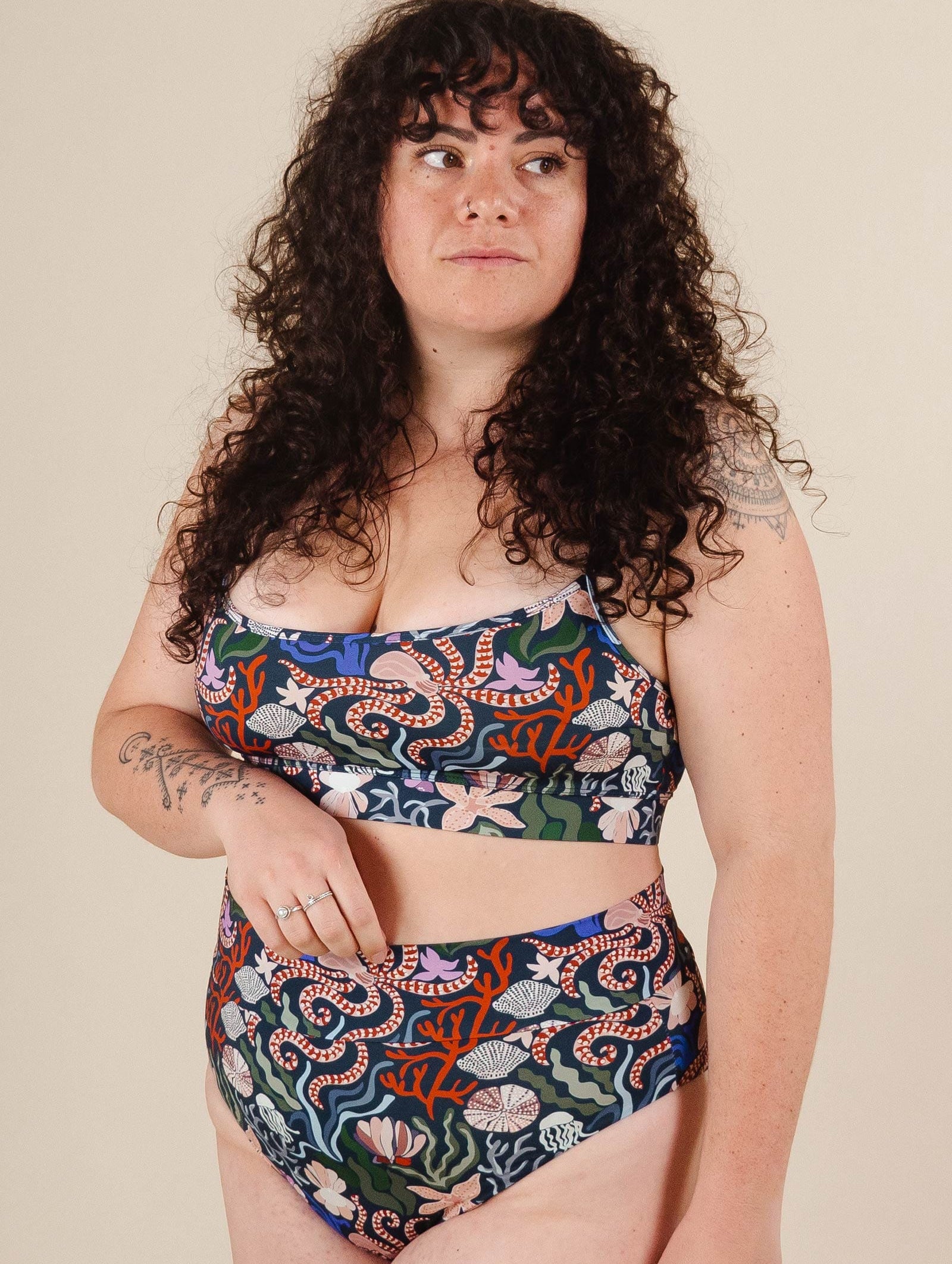 A woman with curly hair wearing a comfortable Coral Bikini Sea Print top from mimi and august.