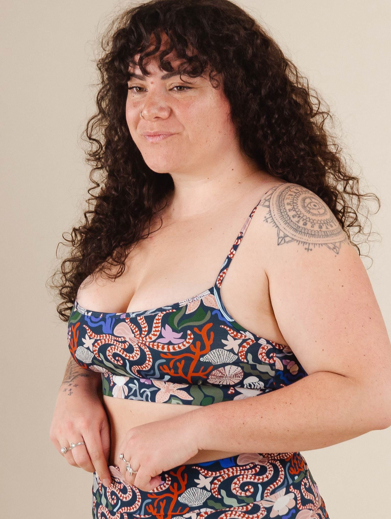 A woman with a tattoo on her arm posing for a picture in the mimi and august Mango Oceana Bralette Bikini Top.
