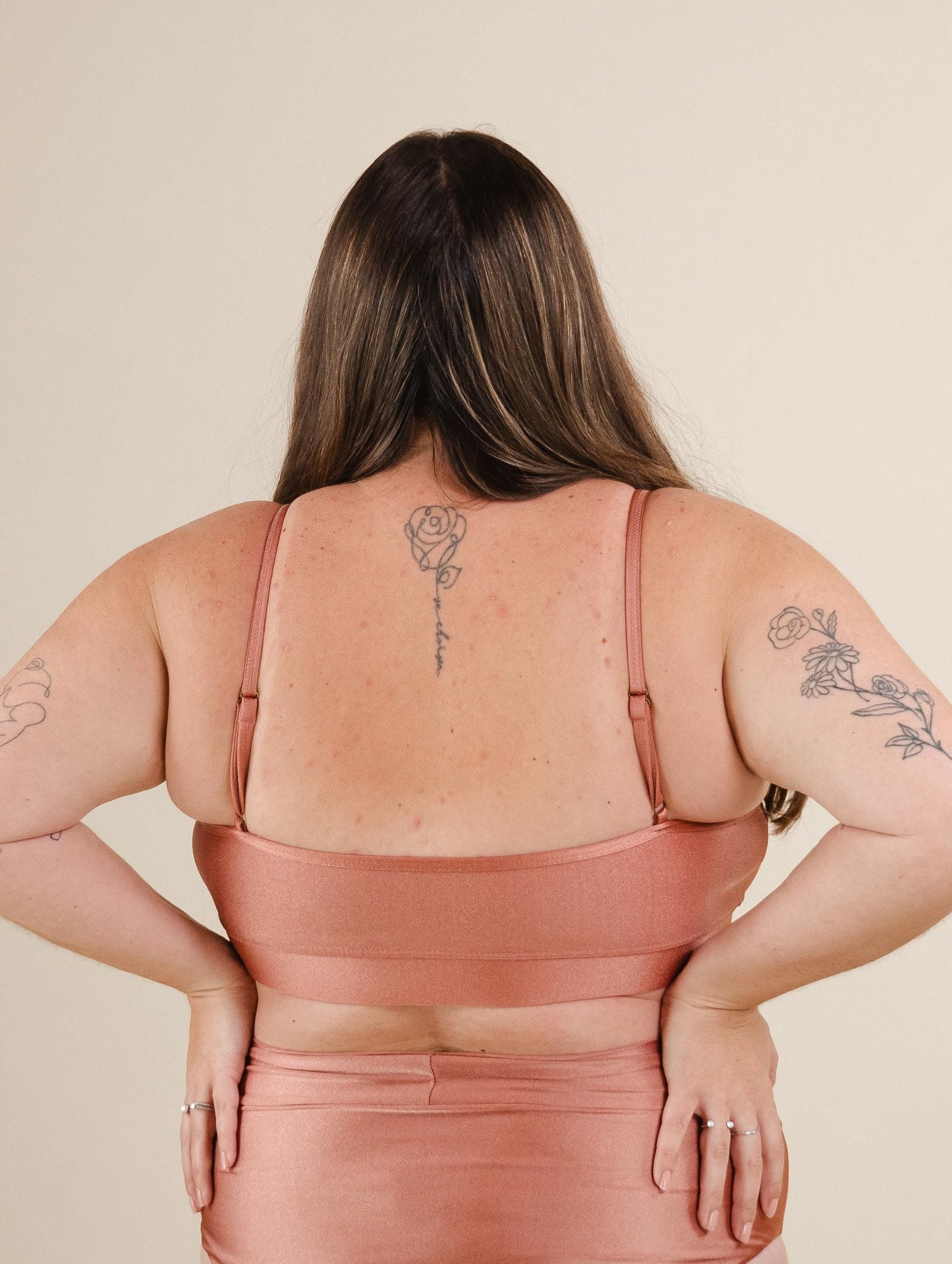 A woman wearing a Mango Sunset Bralette Bikini Top with a rose tattoo on her back.