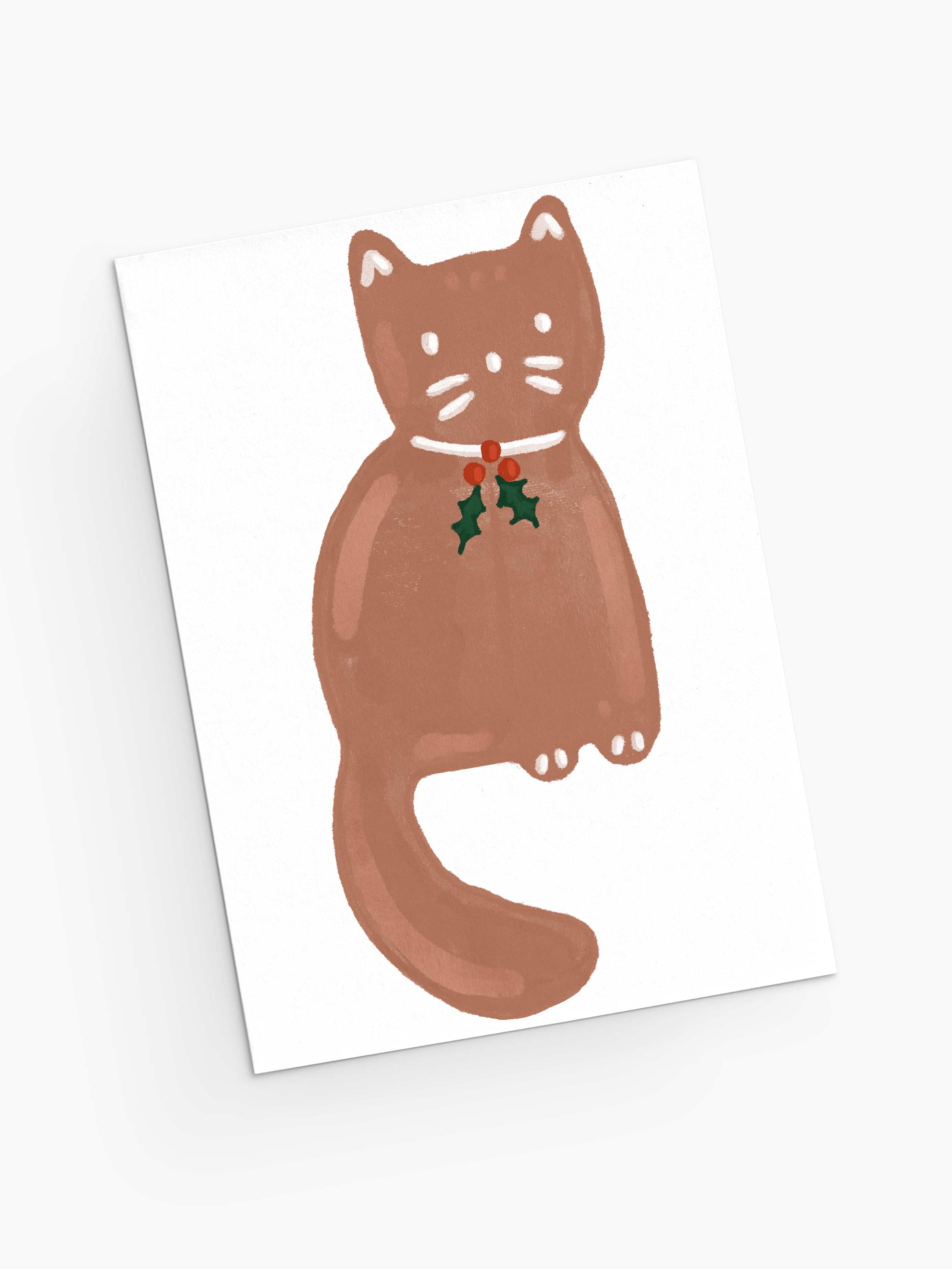 The "Merry Cookie - Christmas Greeting Card" by Mimi & August features an illustration of a brown cat with a red collar and holly leaves, sitting on a white background. It's perfect for holiday greetings and printed on recycled paper.