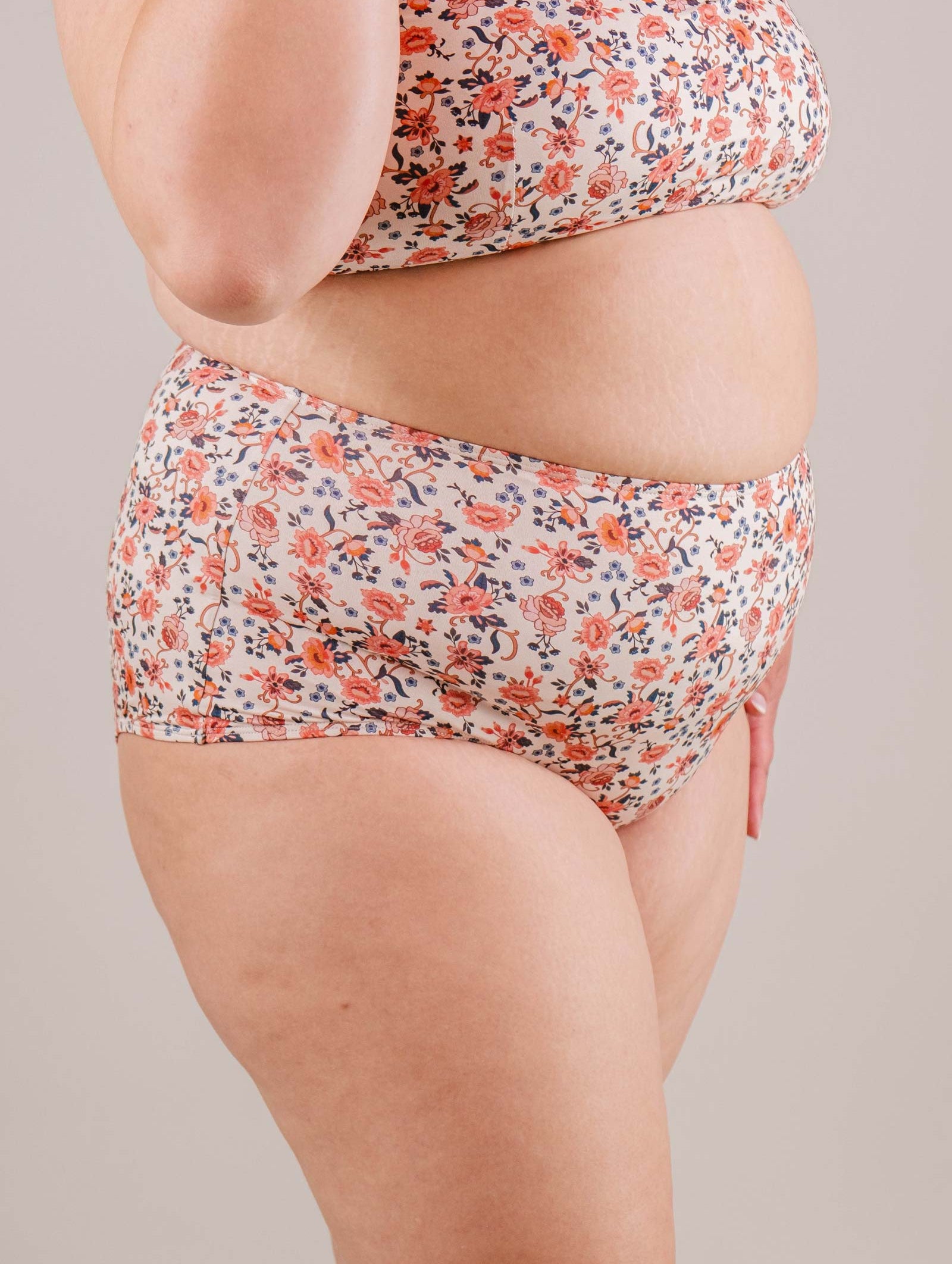 Side view of a plus-size woman wearing a Mimi & August Paloma Amour High Waist Bikini Bottom, focusing on the torso and upper thighs against a neutral backdrop.
