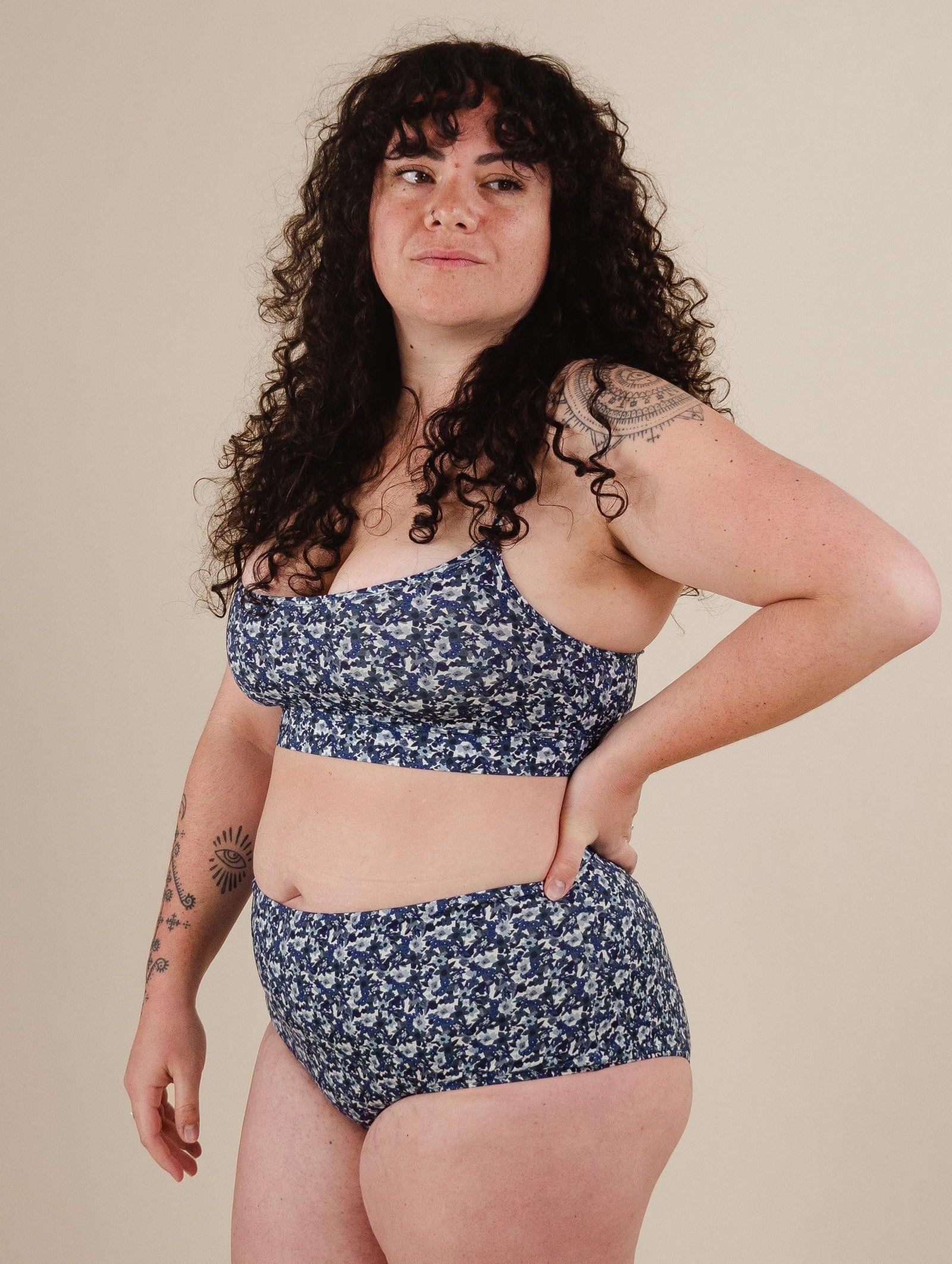 a woman wearing Paloma Moonflower High Waist Bikini Bottom with a tattoo on her right arm.