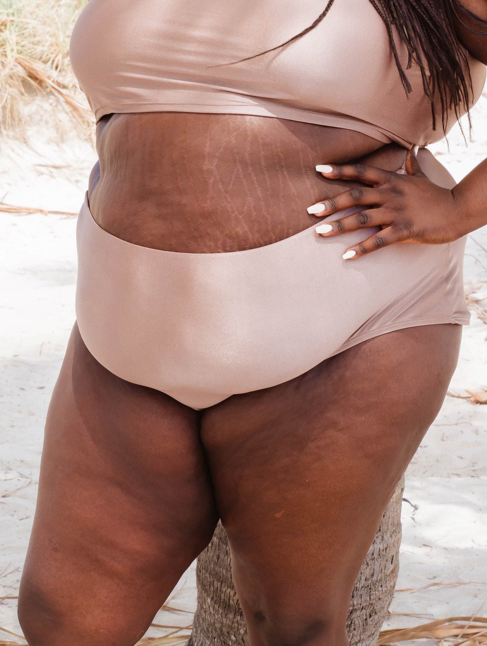 Close up at a sand beige shade bikini bottom worn by a woman standing in miami beach.