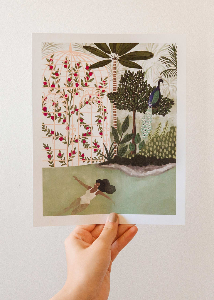 A hand holding up an illustration of a woman in the water, featuring the Peacock Garden illustration by mimi and august.