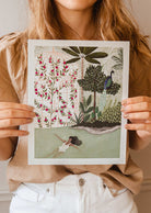 A girl holding up a Peacock Garden Art Print by mimi and august.