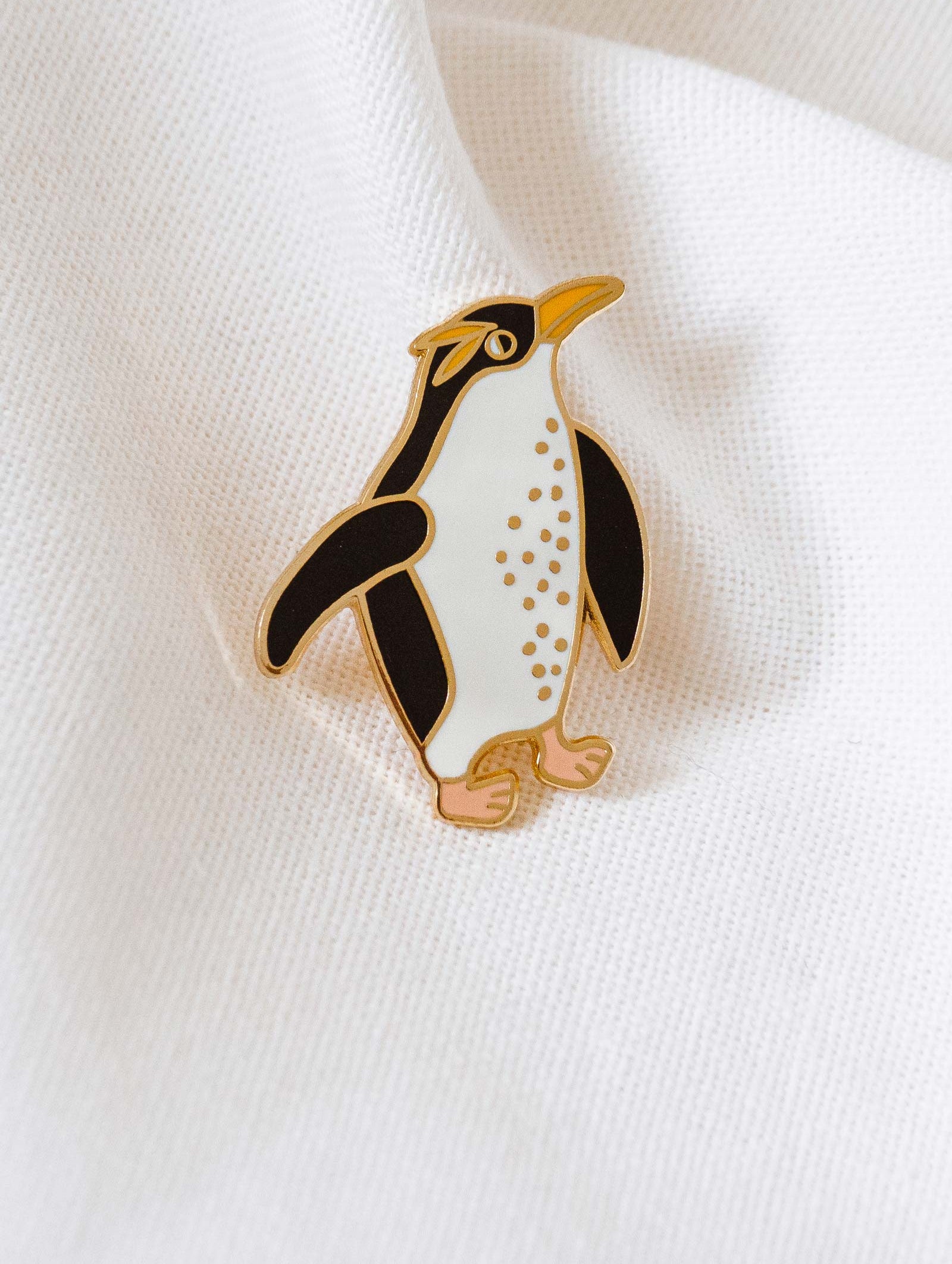 A winter-themed penguin enamel pin by mimi and august on a white shirt
