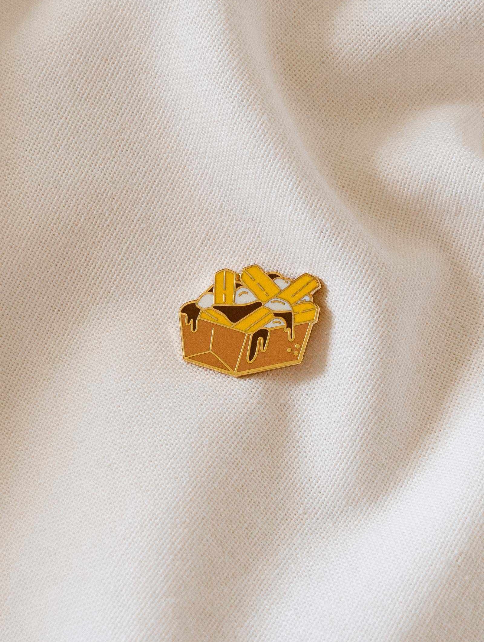 Poutine enamel pin featuring fries, cheese curds, and gravy design in gold tone brass, 38mm size, designed in Montreal