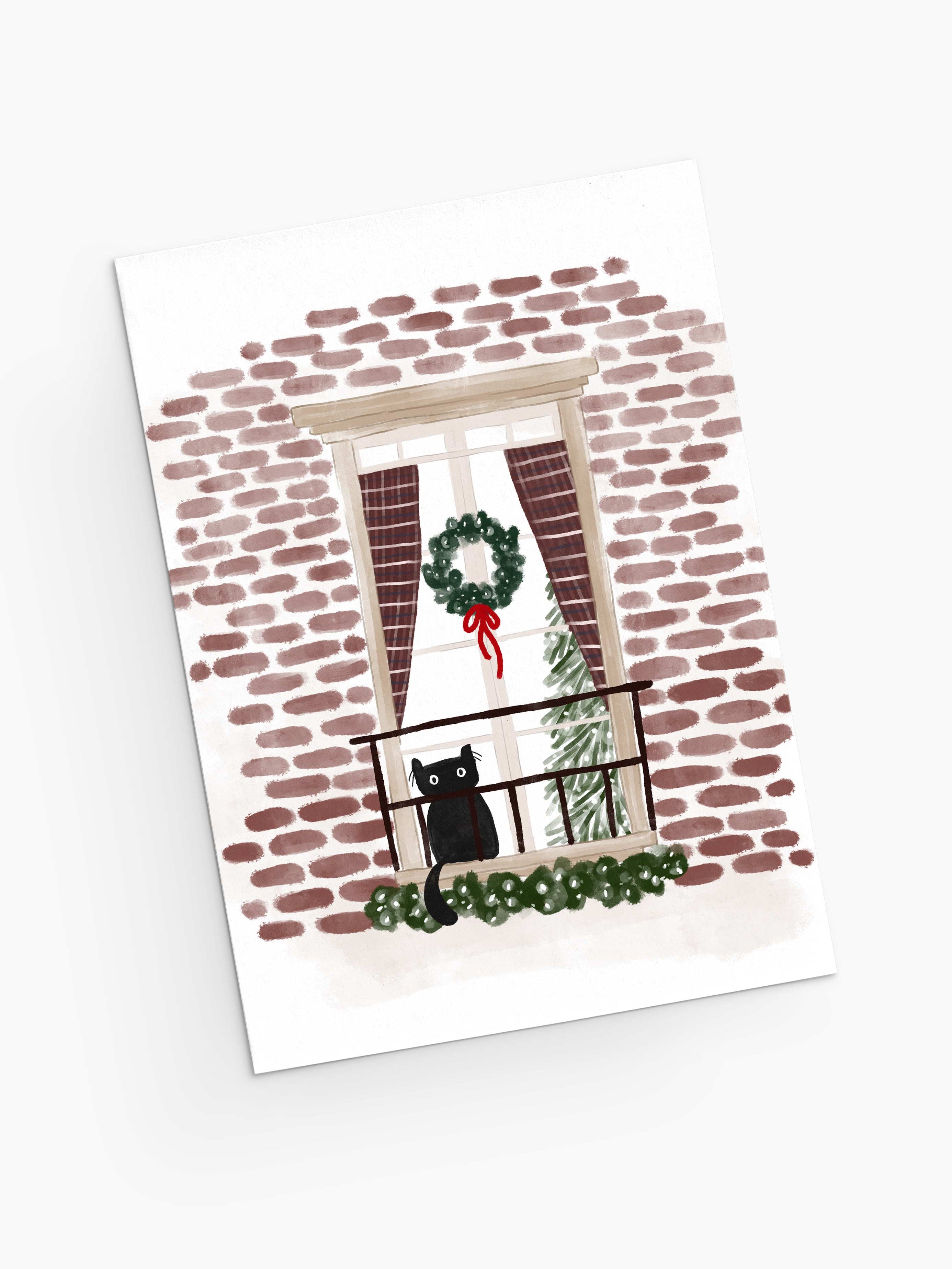 Purr-fectly Waiting for Santa - Christmas Greeting Card by Mimi & August features a charming illustration of a black cat perched on a balcony railing, surrounded by festive elements like a wreath and red curtains against a brick wall. Inside the window, a twinkling Christmas tree adds to the holiday spirit. This beautifully designed card is made with recycled paper and packaged in compostable materials.