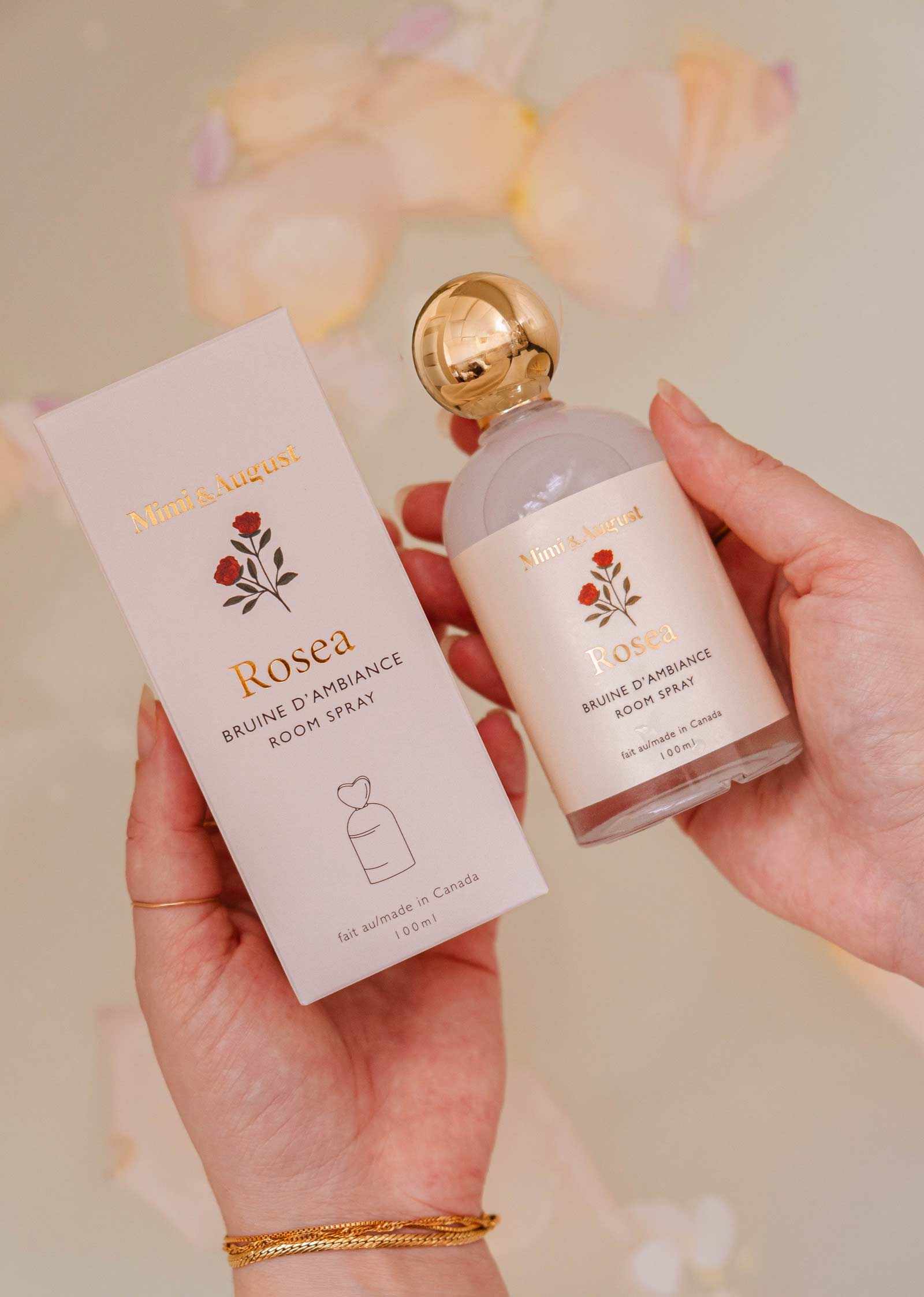 A person holds the Mimi & August Room Spray - Rosea, a citrus floral scent with minimalist floral designs and gold accents—ideal for enhancing any home fragrance collection.