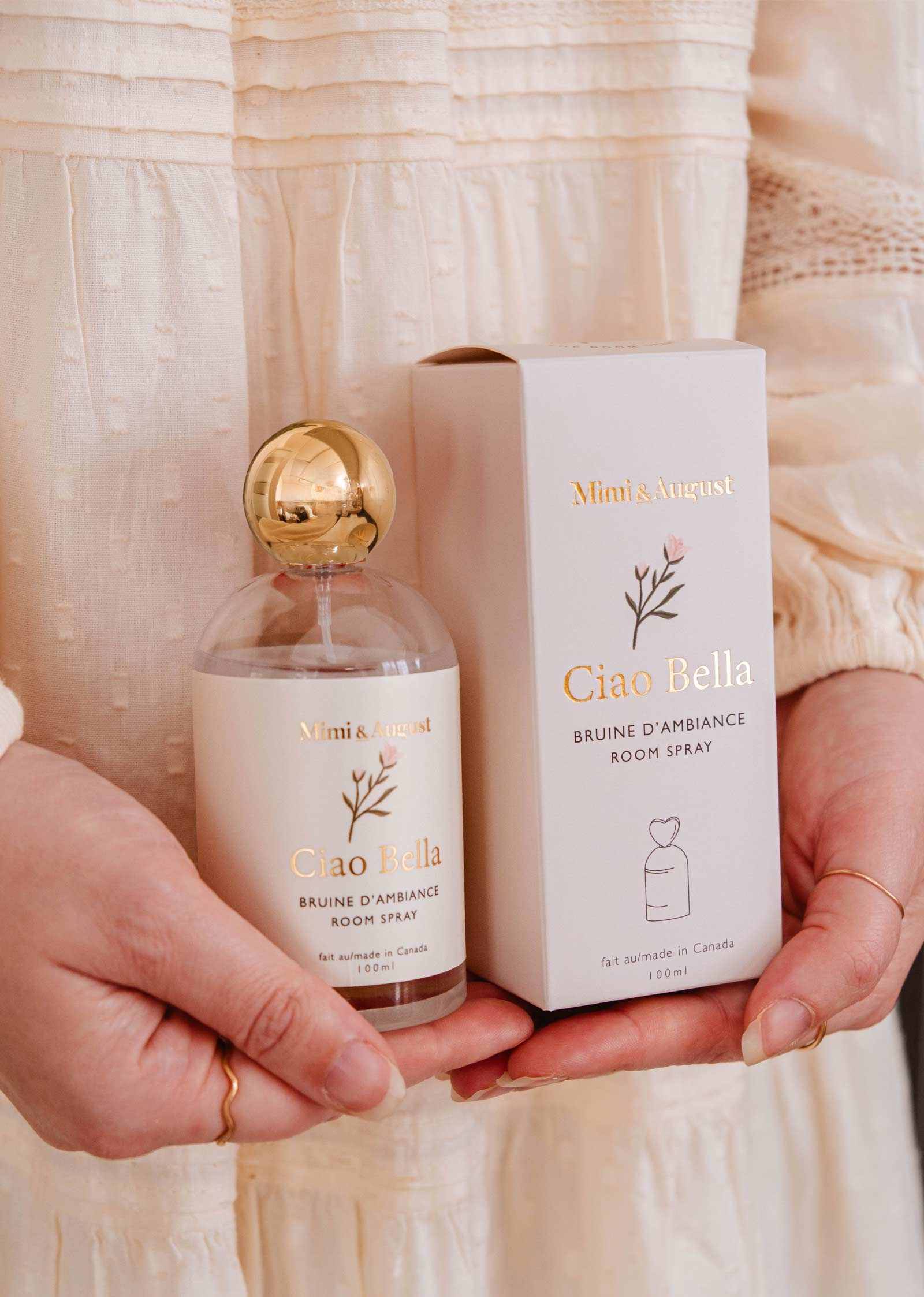 A person holds Mimi & August’s Room spray - Ciao Bella, packaged in minimalist beige and gold—a chic home fragrance that fills spaces with a soft floral aroma.