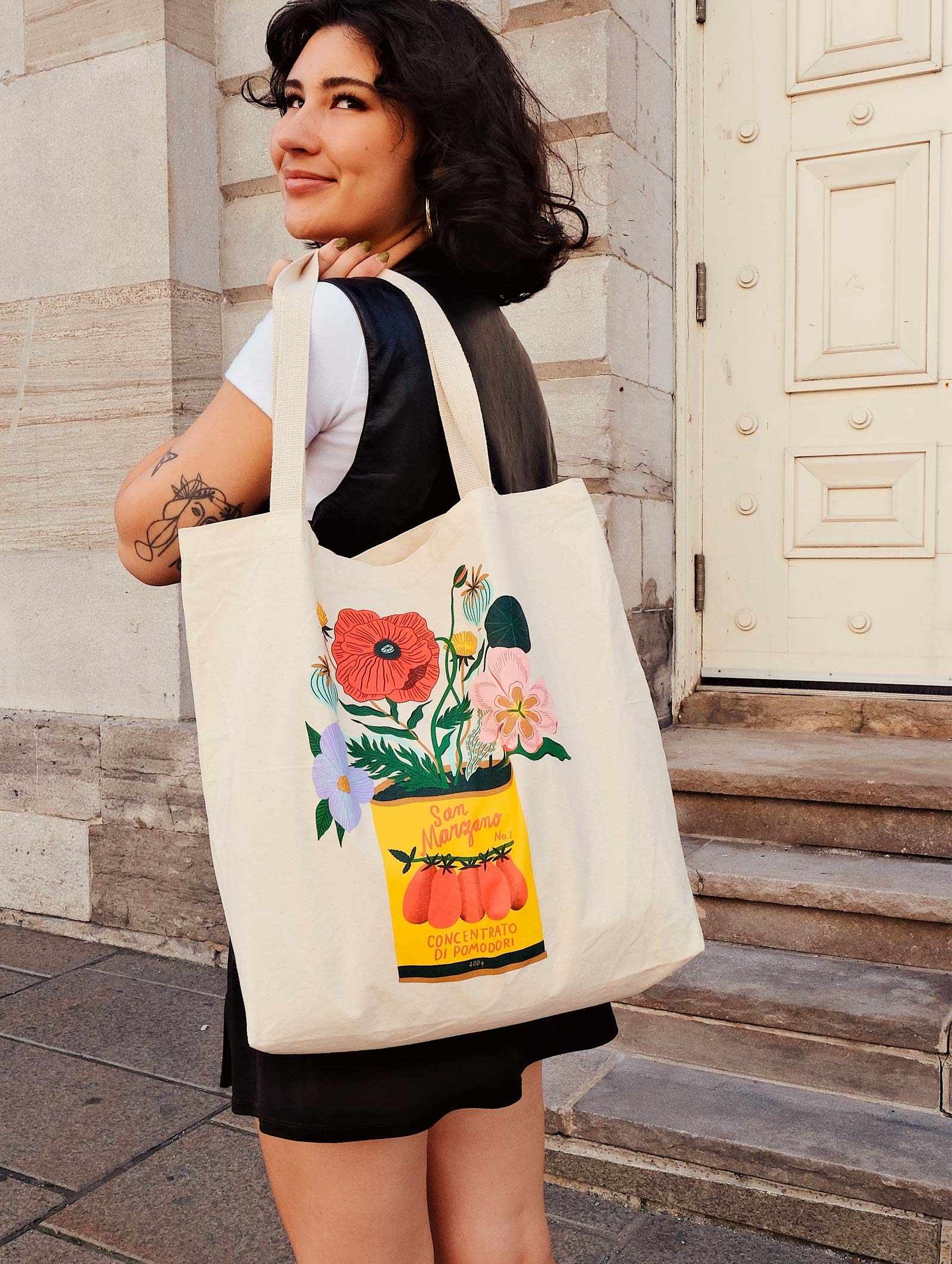 A woman holding a mimi and august Natural tote bag with flowers on it.