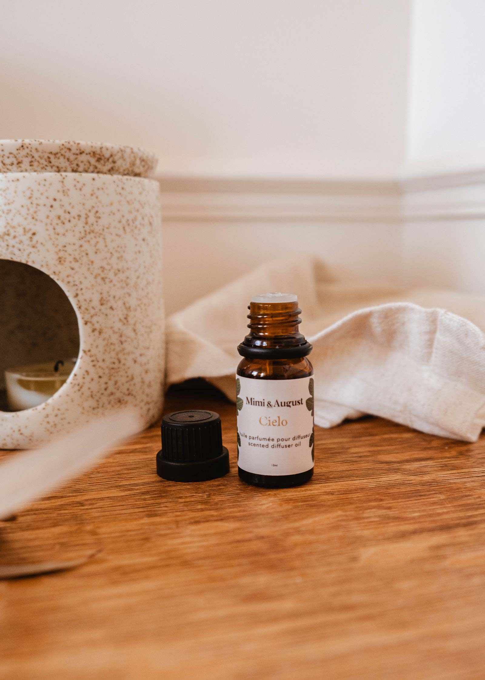 Bouteille brune d'huile parfumée figue Cielo de Mimi & August, bouchon retiré, à côté d'un diffuseur en céramique.