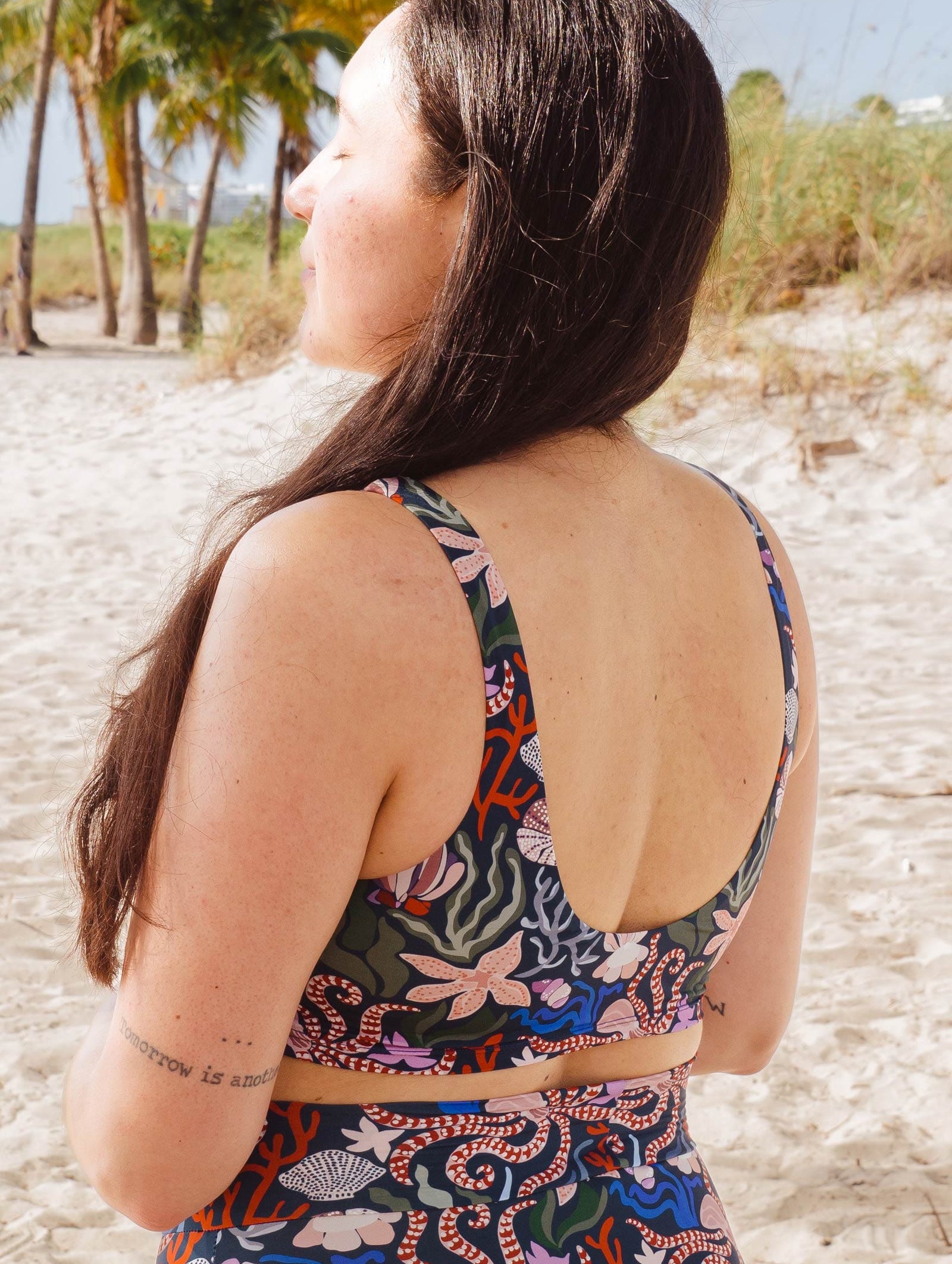 A woman in Mimi beach meditating and wearing the oceana tahiti bikini top by mimi and august