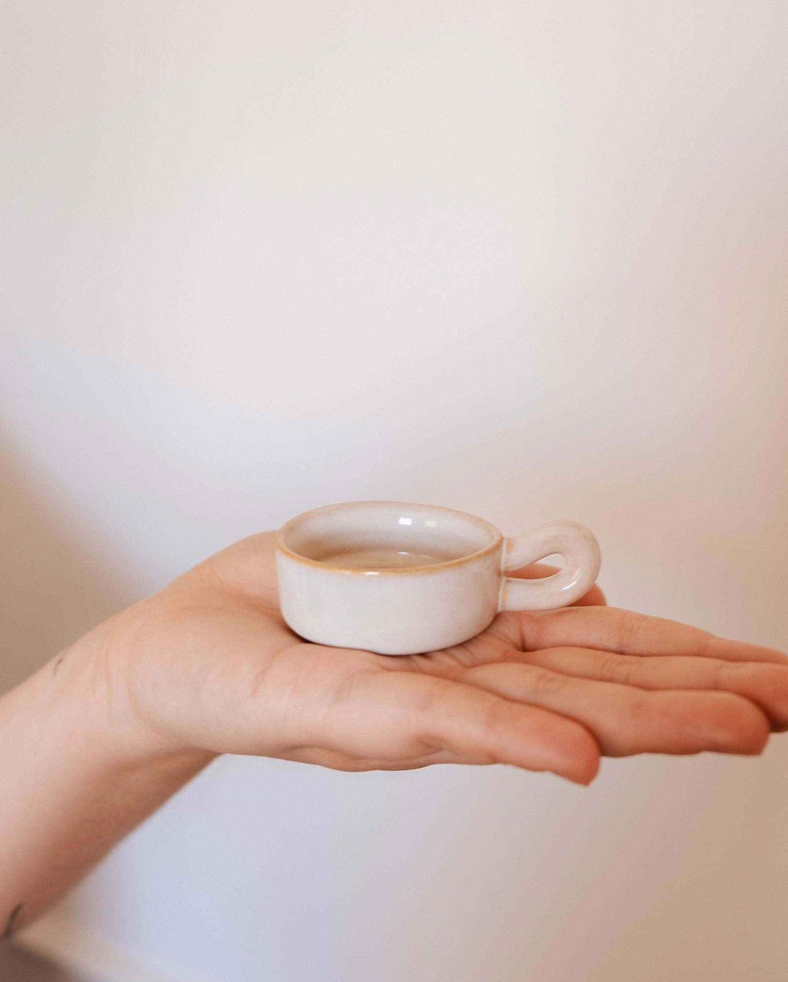 The Mimi & August Tealight Holder, a small white ceramic piece, is displayed on an open palm against a plain background—perfect for adding charm to any rustic decor.
