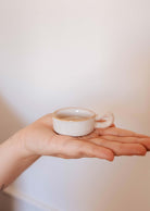 The Mimi & August Tealight Holder, a small white ceramic piece, is displayed on an open palm against a plain background—perfect for adding charm to any rustic decor.