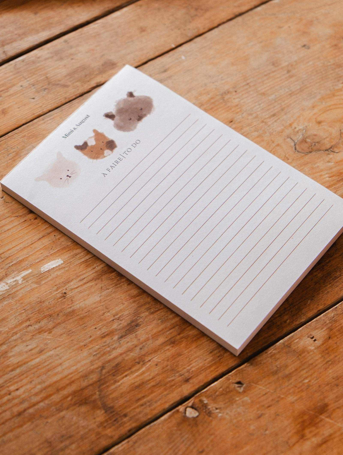 The Purrfect - Notepad by Mimi & August features lined pages with cartoon animal faces, including a kitty illustration at the top, making it a cute stationery item for your desk.