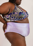 Person shown from the side, wearing a patterned sports bra and Mimi & August Tofino Lilac High Waist Bikini Bottom.