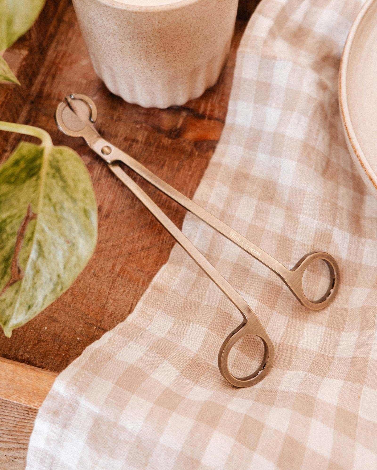 A Mimi & August Wick Trimmer rests on the table, its stainless steel design perfect for trimming candle wicks with ease.
