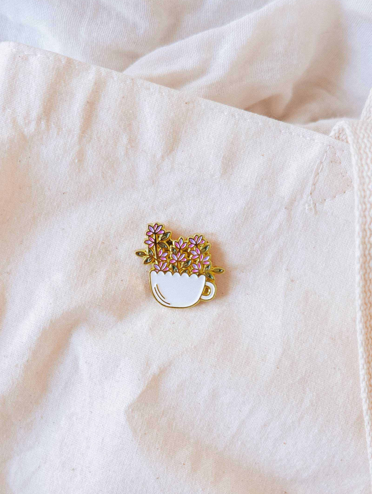 Épinglette Tasse Fleurie mettant en vedette une tasse dorée débordante de fleurs, symbole de joie, d’épanouissement et de croissance