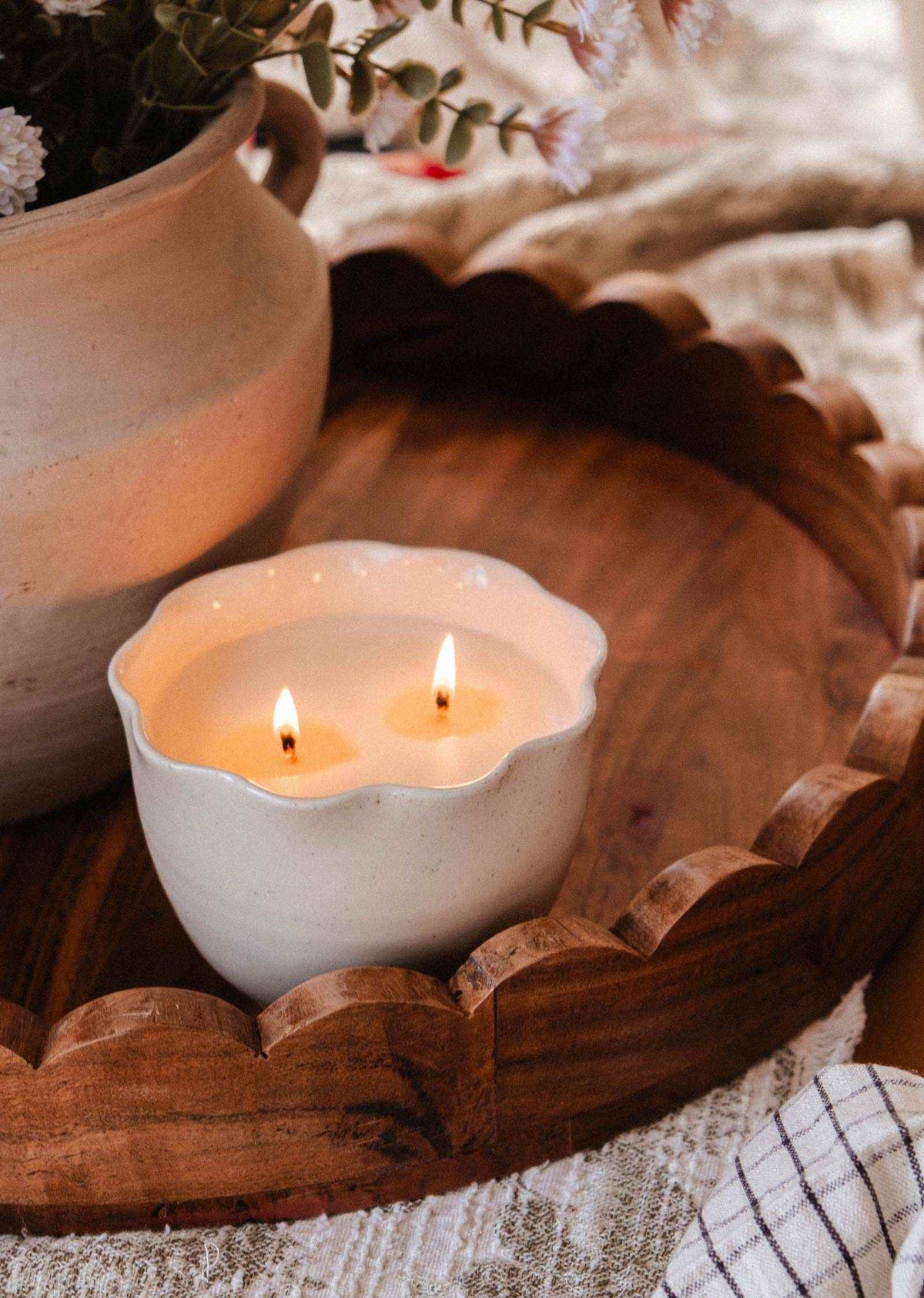Ceramic bowl candle in a speckled cream glaze, with a scalloped petal-shaped rim and two lit wicks.