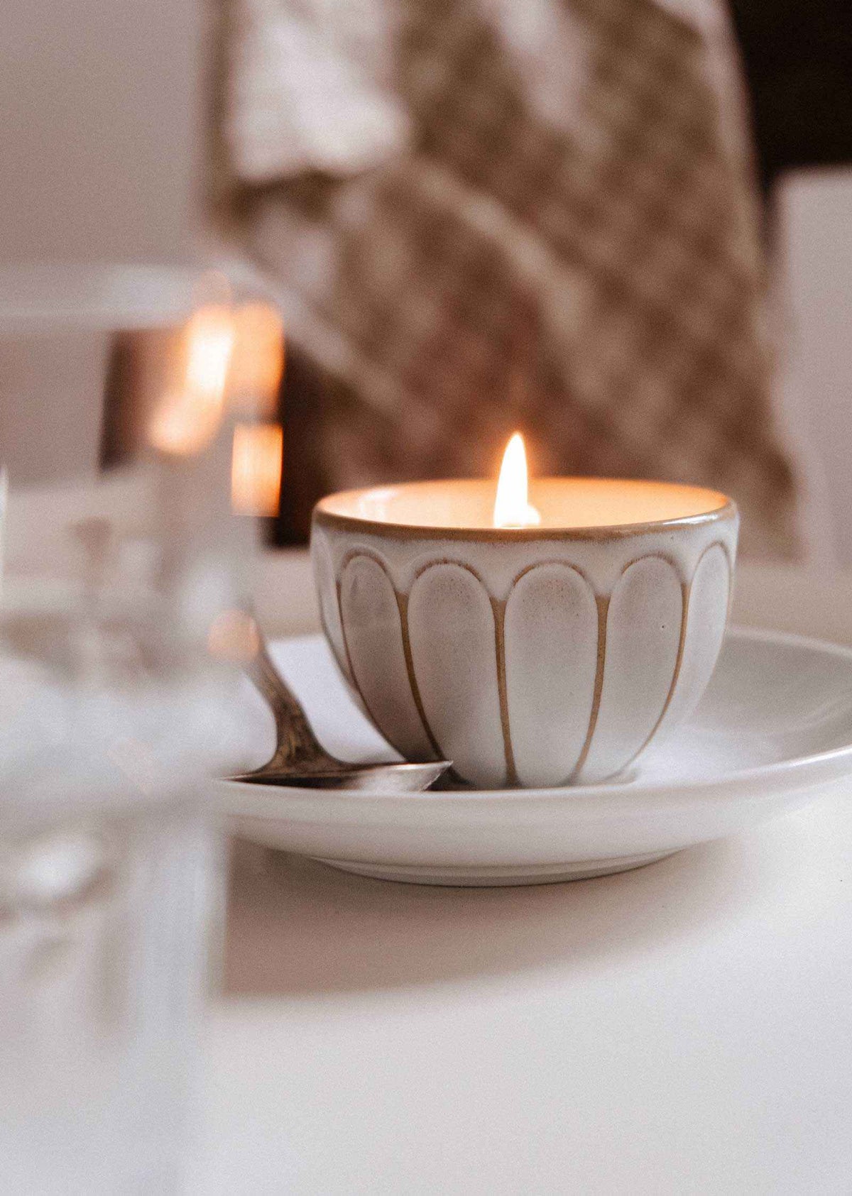 A lit Le Petit Café Mimi – Two Little Cups Candle in a fluted ceramic cup sitting on a matching saucer.