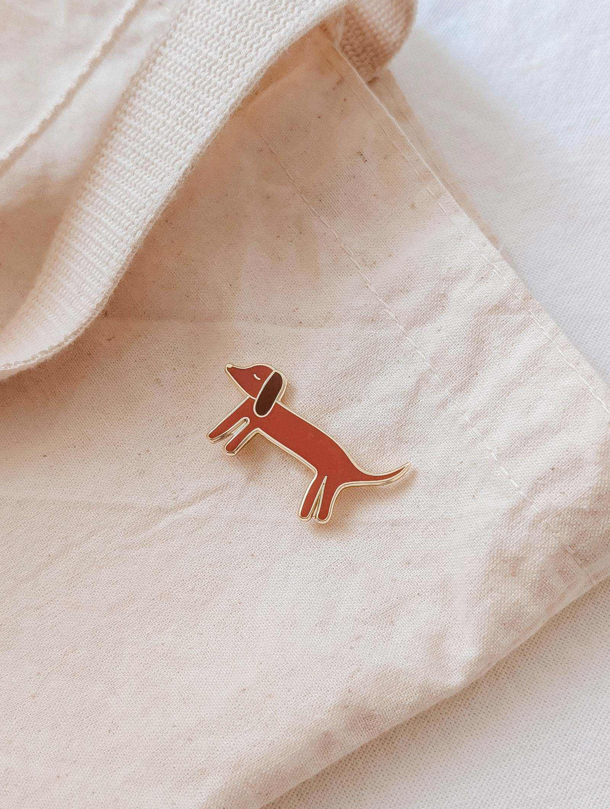 Épinglette Dachshund représentant un teckel au corps allongé, en laiton doré et émail aux tons chauds.