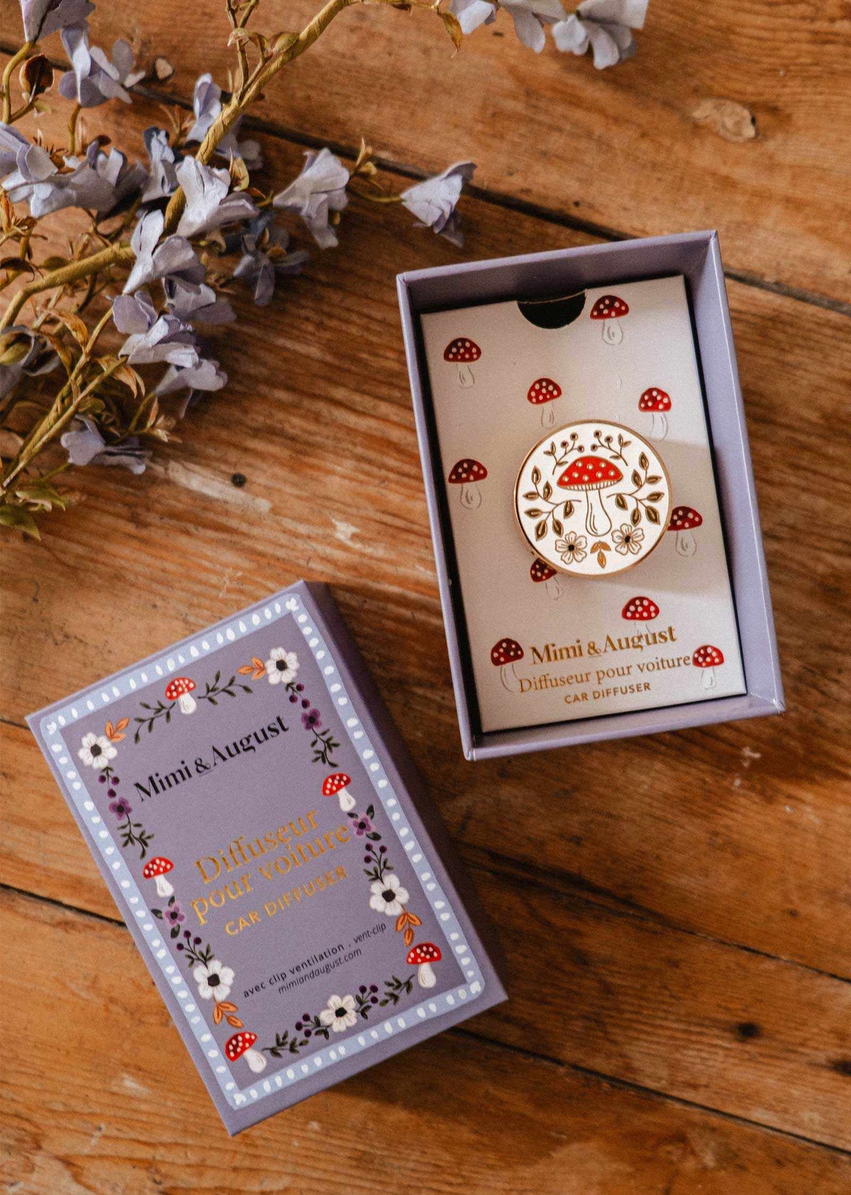 Diffuseur pour voiture Champignon en émail crème et doré, décoré d’un champignon rouge et de fleurs, dans son coffret illustré.