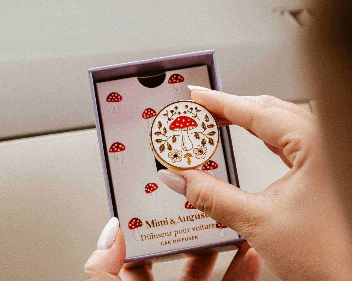 Diffuseur pour voiture Champignon en émail crème et doré, orné d’un motif de champignon rouge, de fleurs et de feuillages.