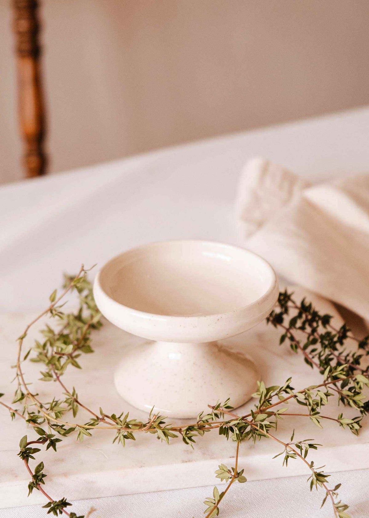 Ceramic pillar candle holder with a glossy ivory finish, shallow round bowl, and short pedestal base