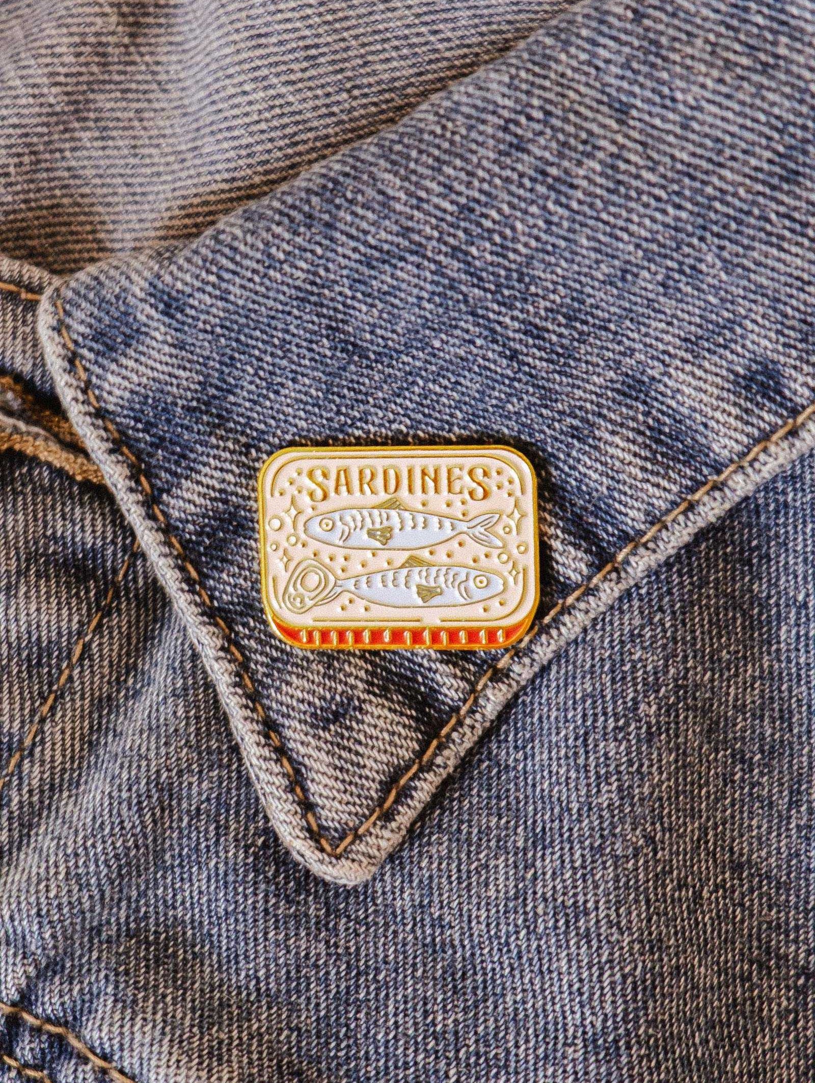 The Cozy Sardines Enamel Pin by Mimi & August, designed in Montreal, adds a touch of personality and charm to your jean pocket.