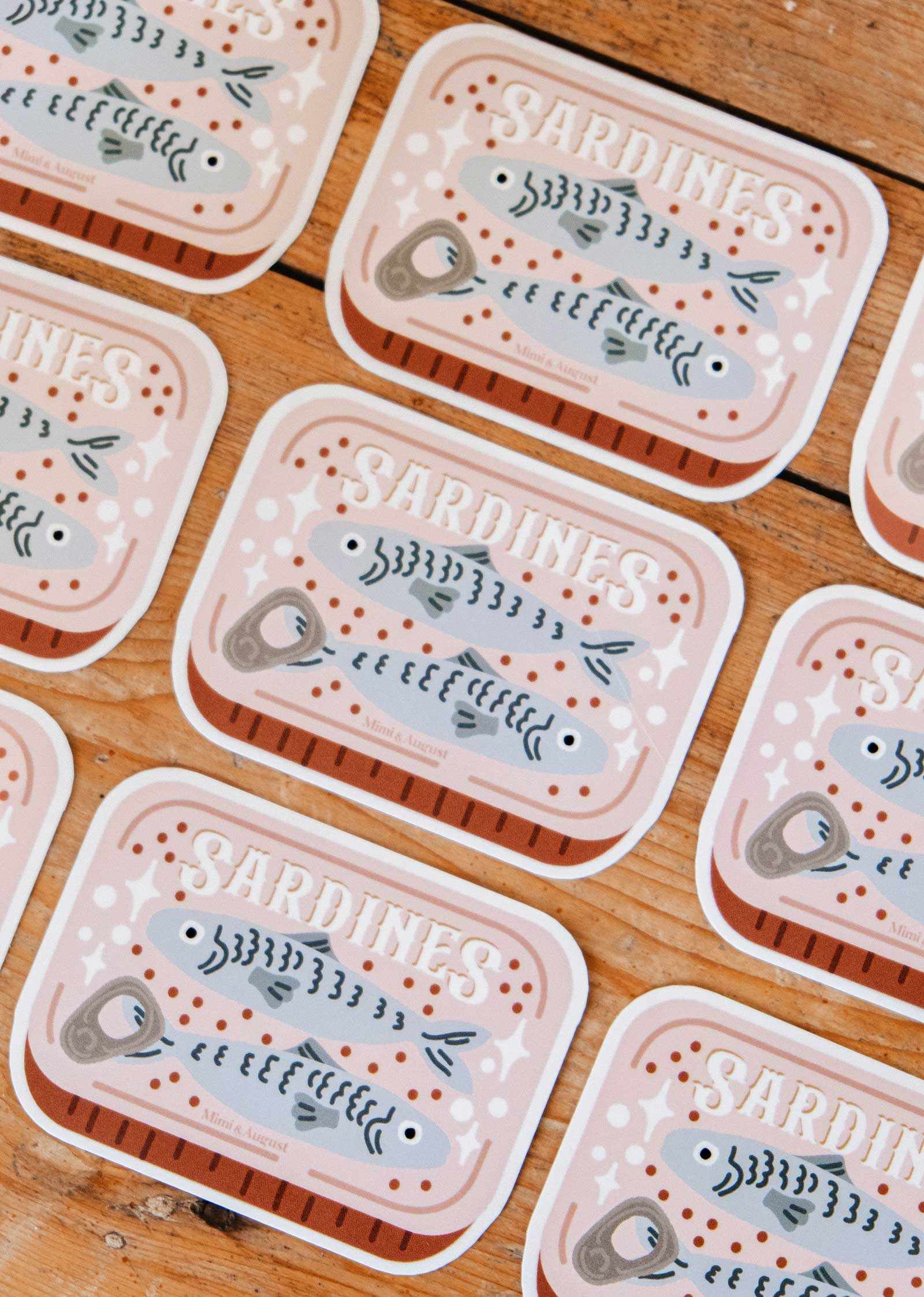 The Cozy Sardines - Vinyl Sticker by Mimi & August is a durable, waterproof sticker featuring three cute sardines in a can labeled "SARDINES," perfect for adding a cozy touch to your items.