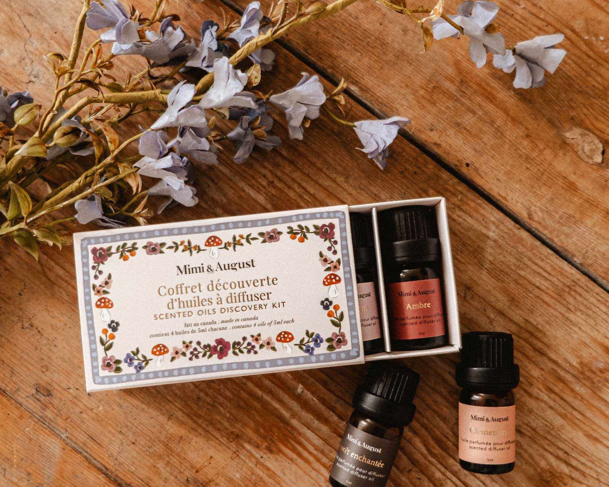 Coffret d’Huiles Parfumées, quatre flacons ambrés avec étiquettes et boîte illustrée à motifs floraux.
