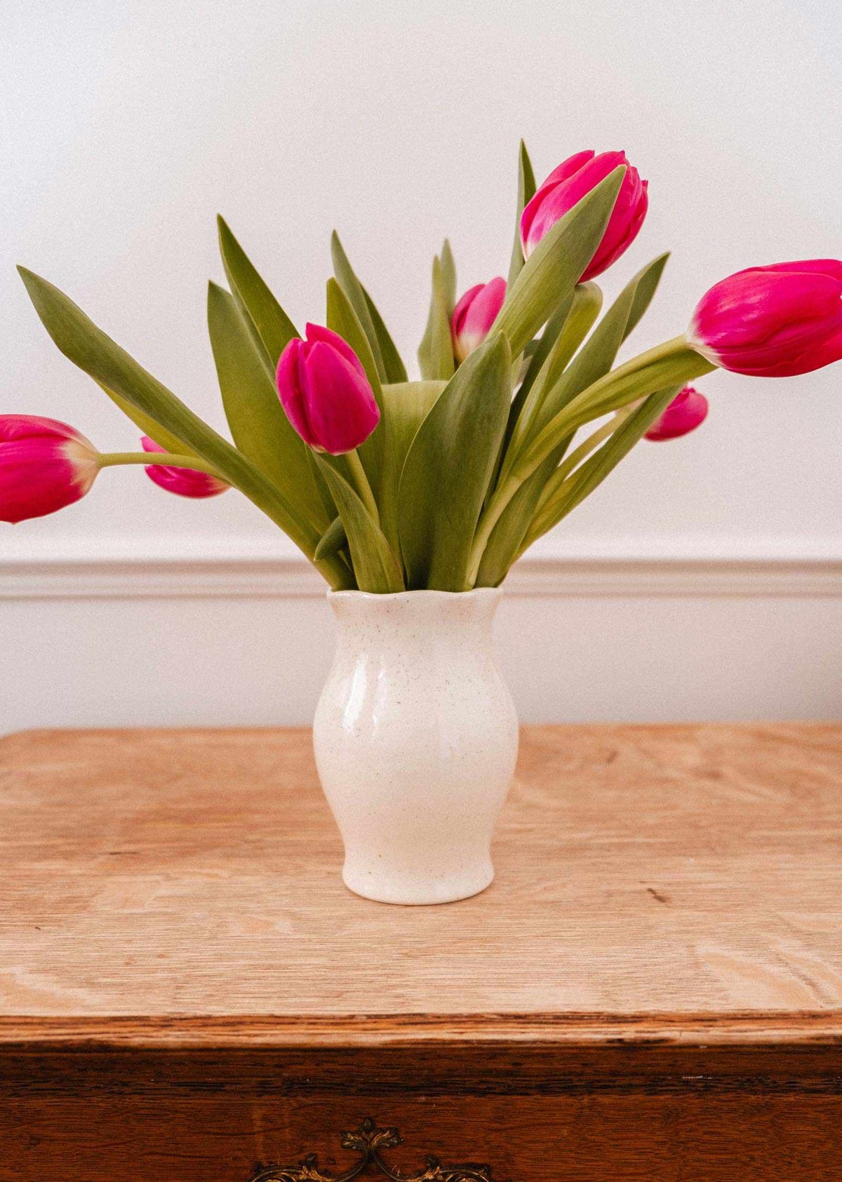Vase Silhouette Ceramic Vase en céramique crème mouchetée, aux courbes douces et au bord ondulé, garni de tulipes roses.