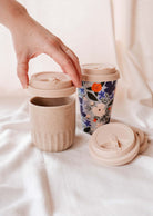 A person holding a recyclable silicone cup with a Mimi Silicone Lid by Mimi & August on it.