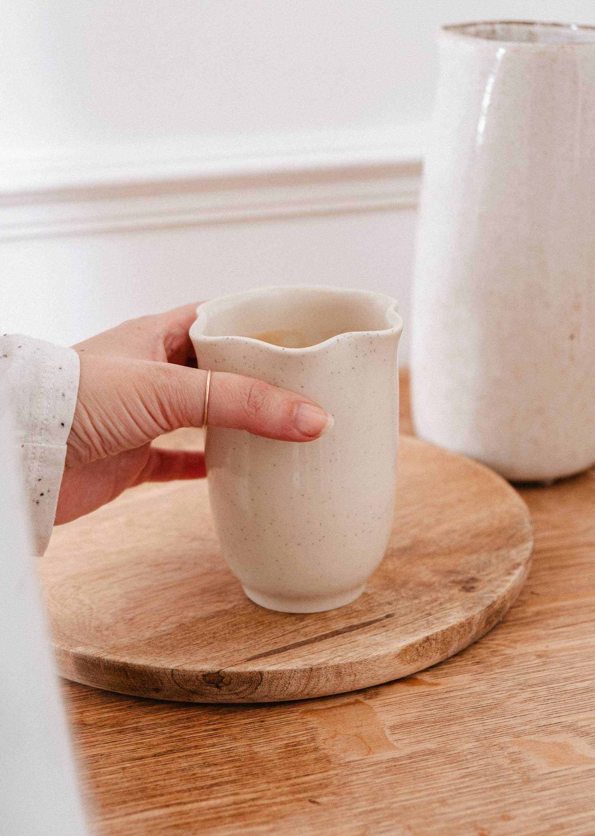 Bougie Orange Épicée dans une tasse en céramique crème mouchetée, au rebord ondulé en forme de pétales, sans anse.