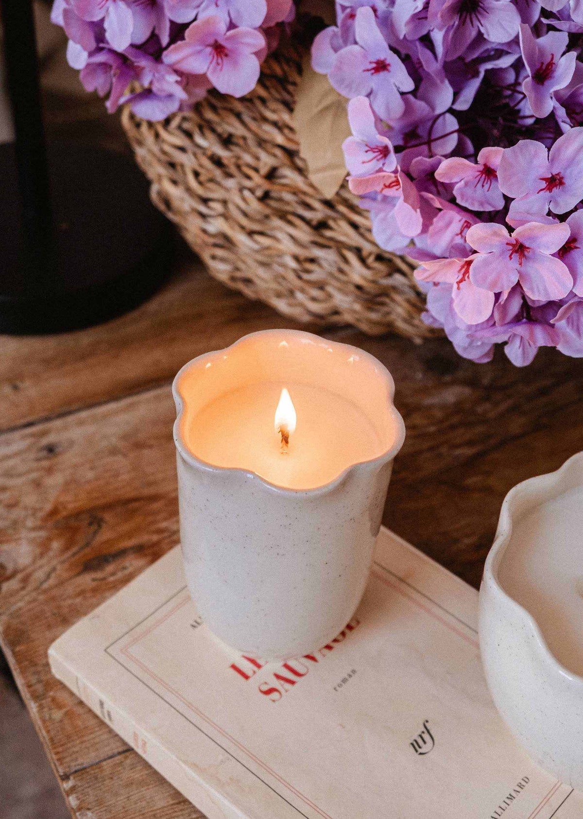 Bougie Orange Épicée dans une tasse en céramique crème mouchetée, au rebord festonné en pétales et à la flamme allumée.