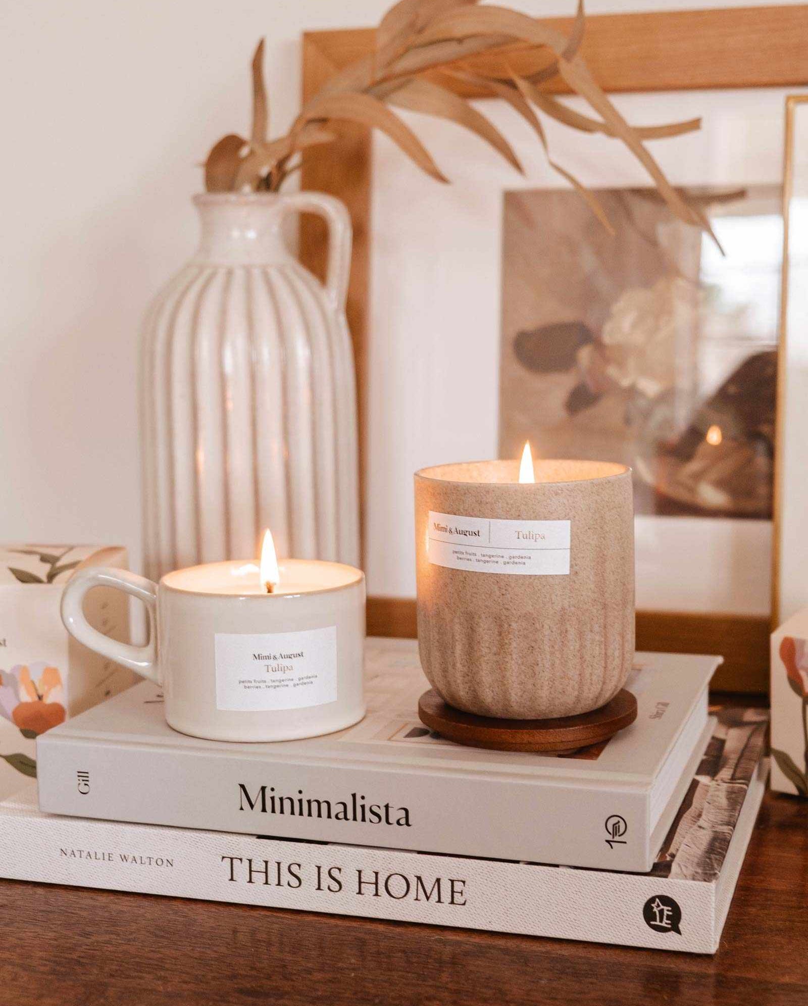 Two Tulipa - Reusable candles on a book titled "minimalista: this is home" with a wooden vase, picture frame, and cup nearby on a table. (Brand Name: Mimi & August)