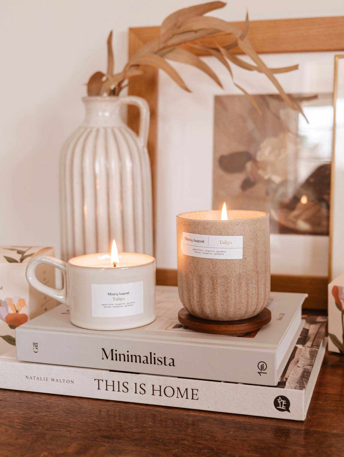 Two Tulipa - Reusable candles on a book titled "minimalista: this is home" with a wooden vase, picture frame, and cup nearby on a table. (Brand Name: Mimi & August)