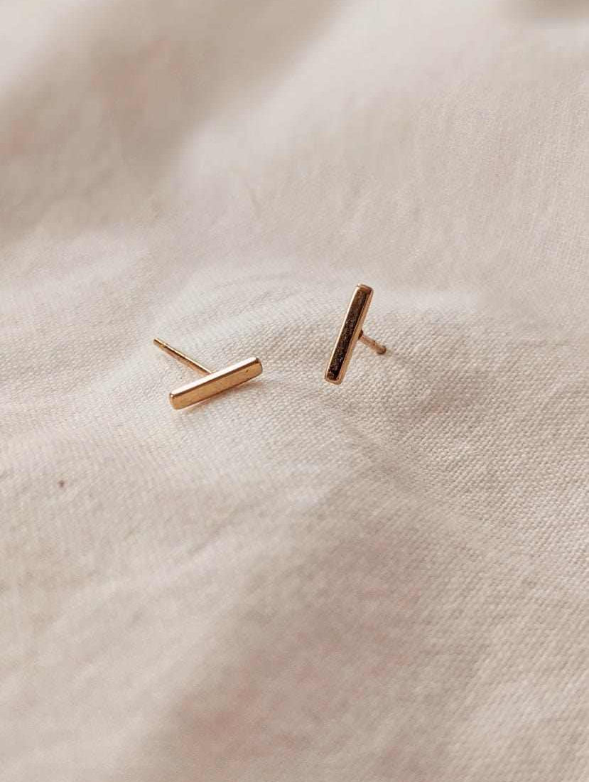 Minimalist gold earrings bar design on fabric background