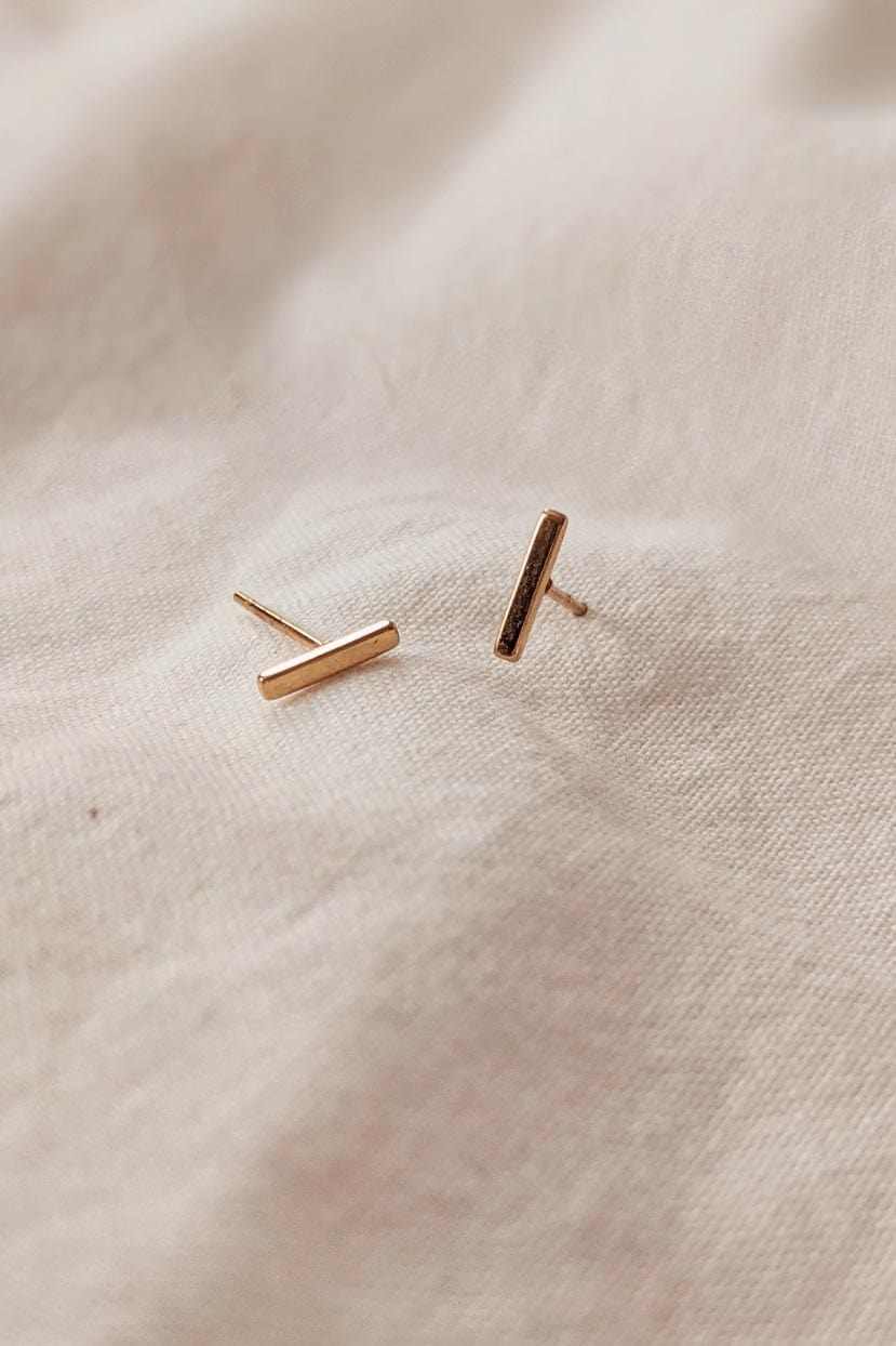 Minimalist gold earrings bar design on fabric background