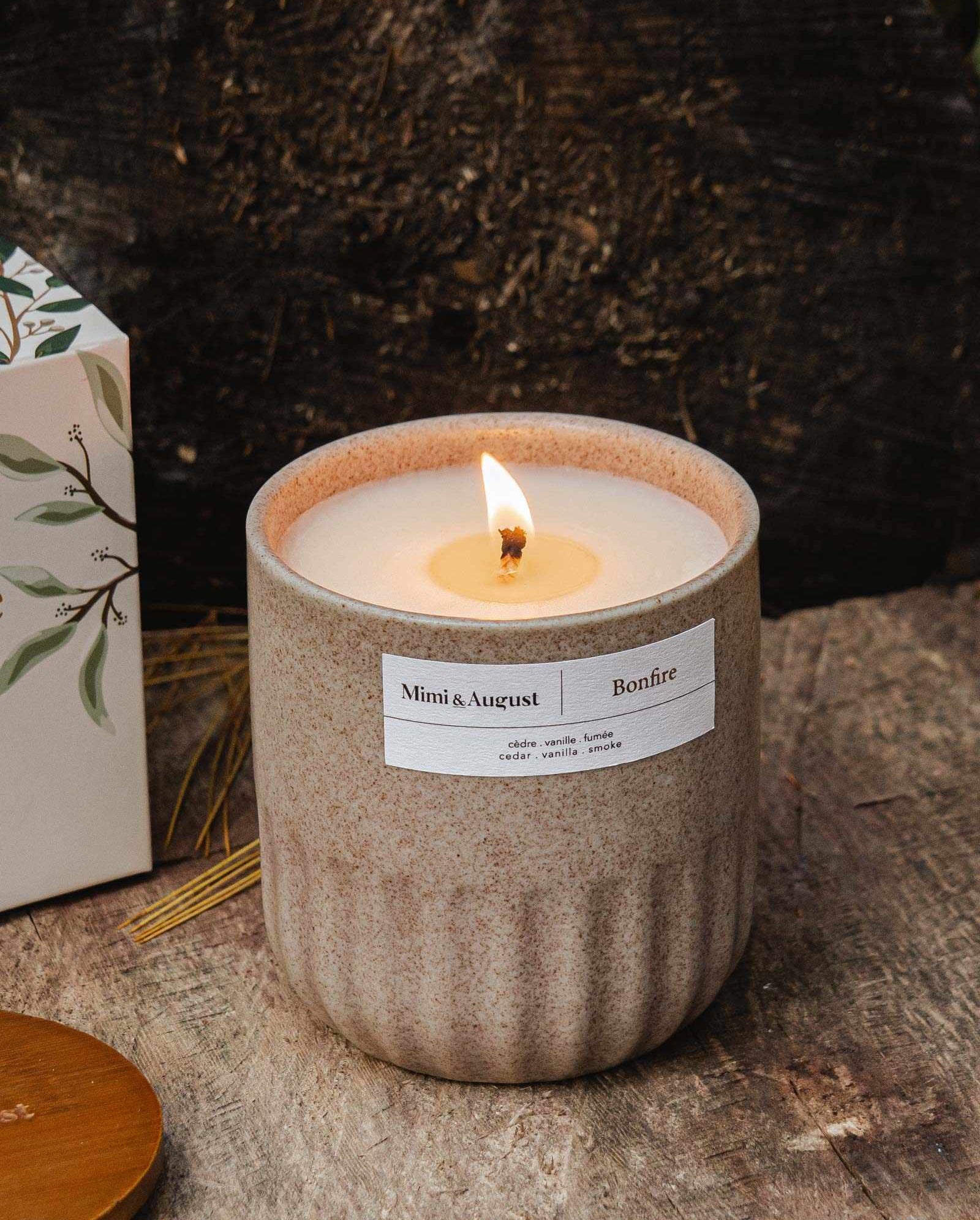 Reusable candle Bonfire with cedar, vanilla, and smoke scent in a speckled gray cup burning on rustic surface