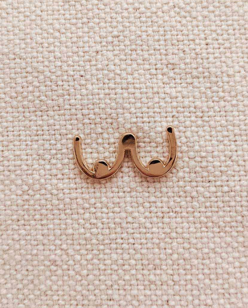 Gold tone boobs enamel pin with minimalist design on textured fabric background
