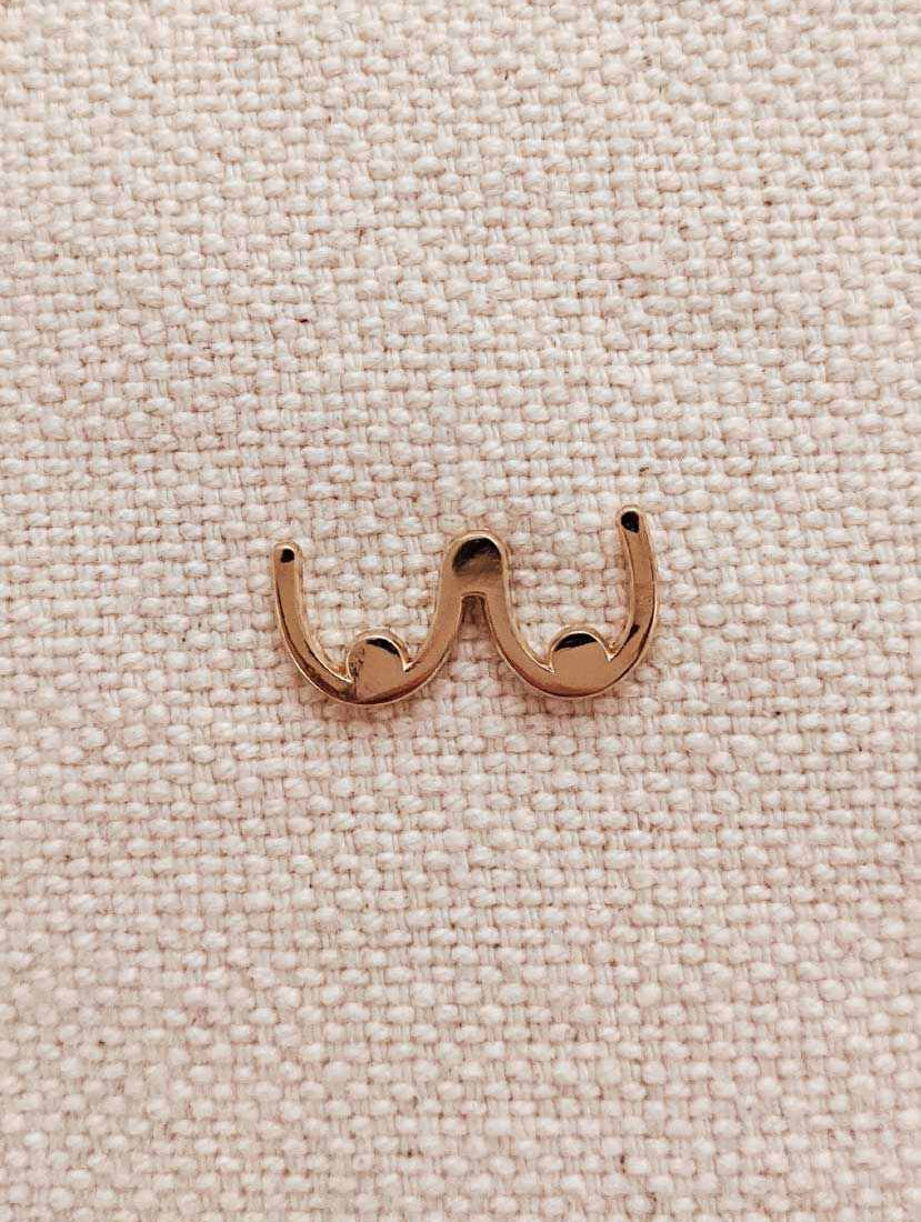 Gold tone boobs enamel pin with minimalist design on textured fabric background