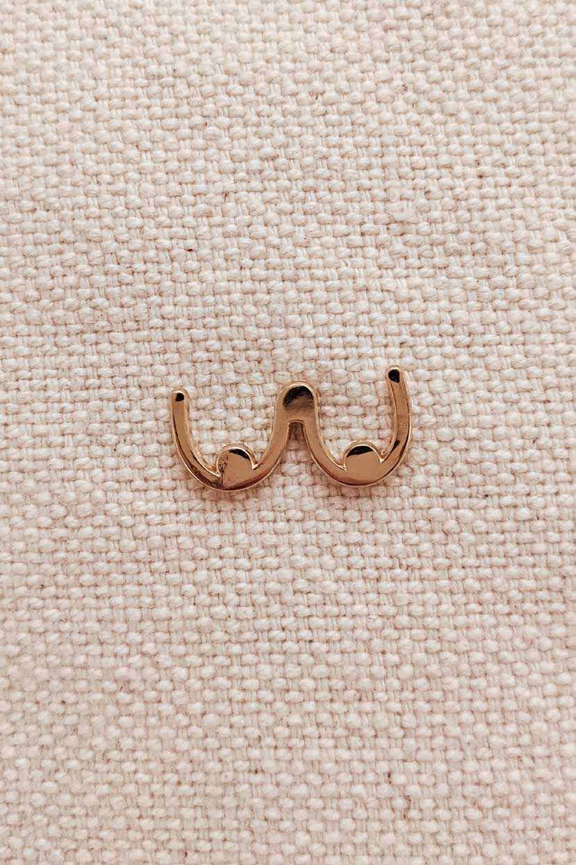 Gold tone boobs enamel pin with minimalist design on textured fabric background