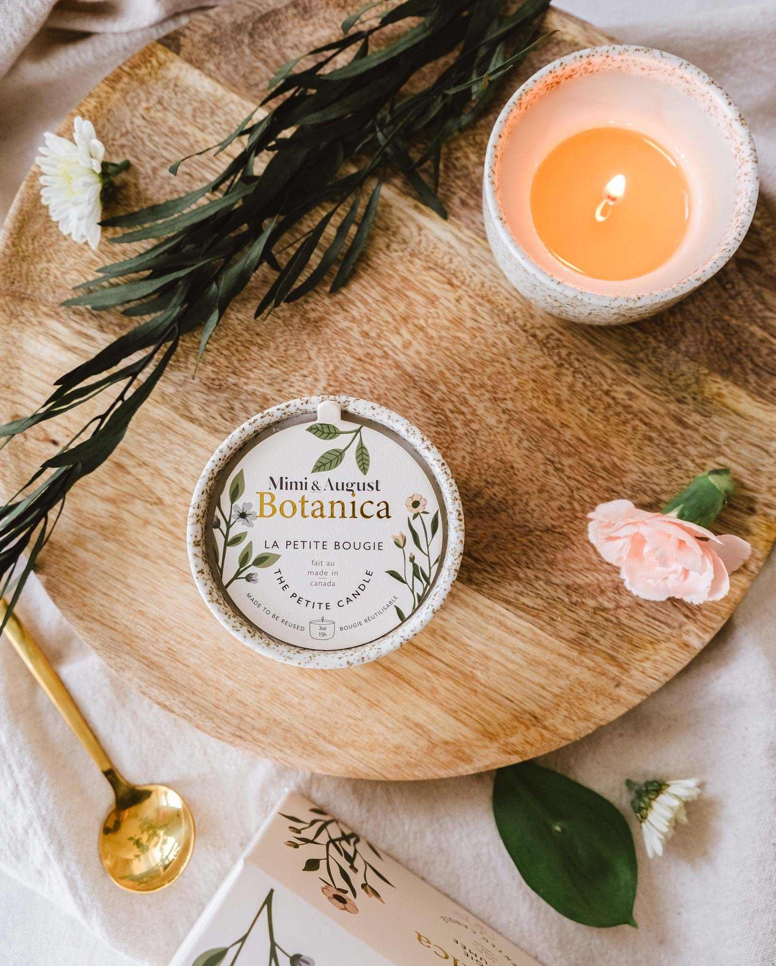 A Mimi & August Botanica - Reusable Candle and a small book placed on a wooden tray decorated with flowers and green leaves, creating a serene ambiance.