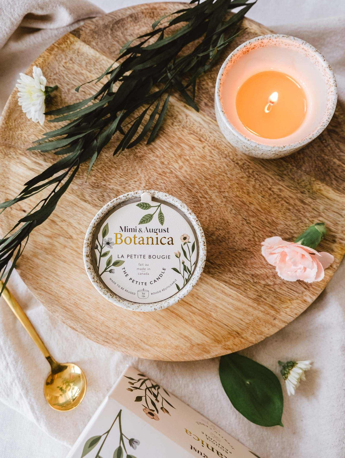 A Mimi & August Botanica - Reusable Candle and a small book placed on a wooden tray decorated with flowers and green leaves, creating a serene ambiance.