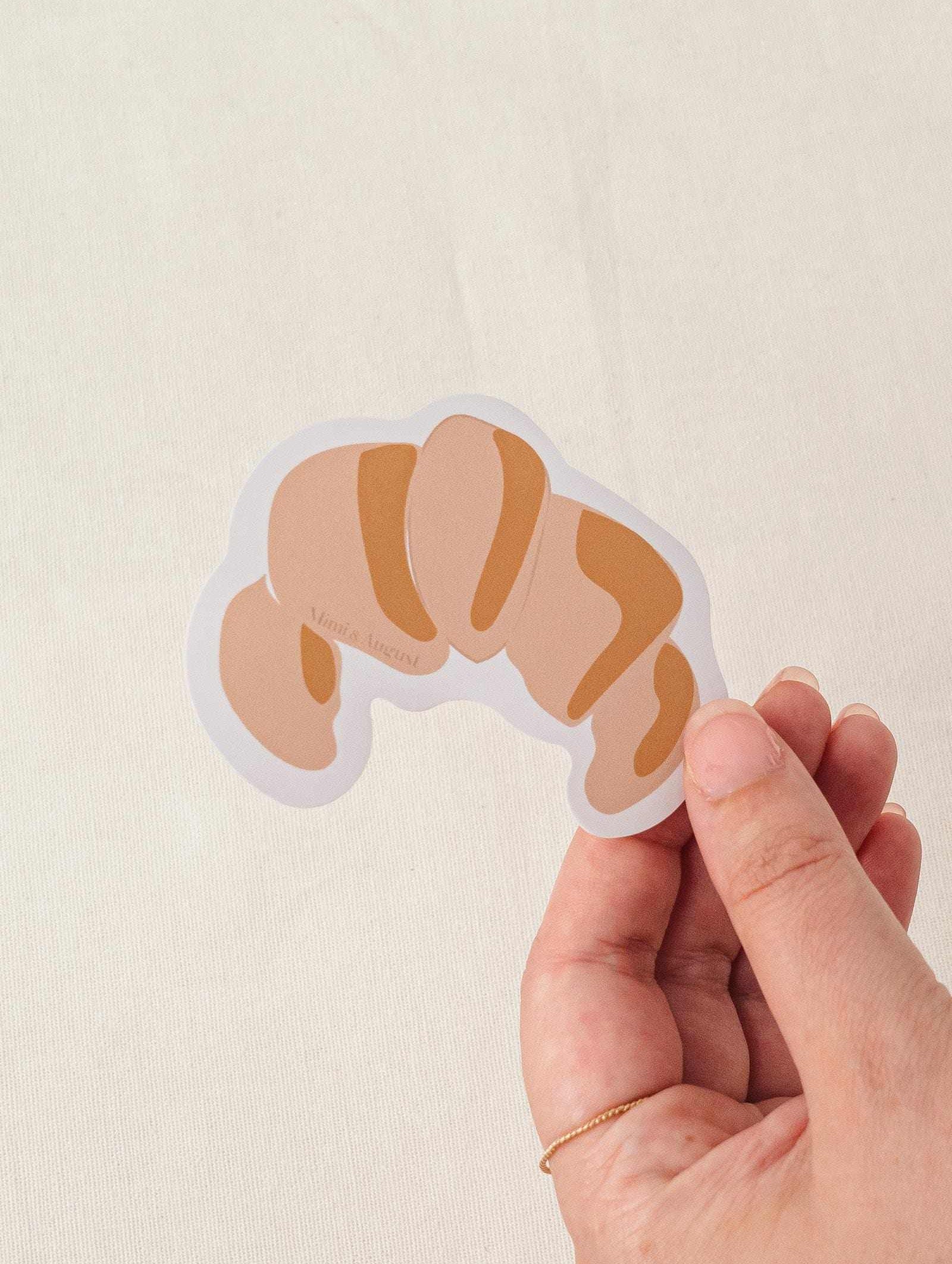 Hand holding croissant vinyl sticker with matte finish and white border