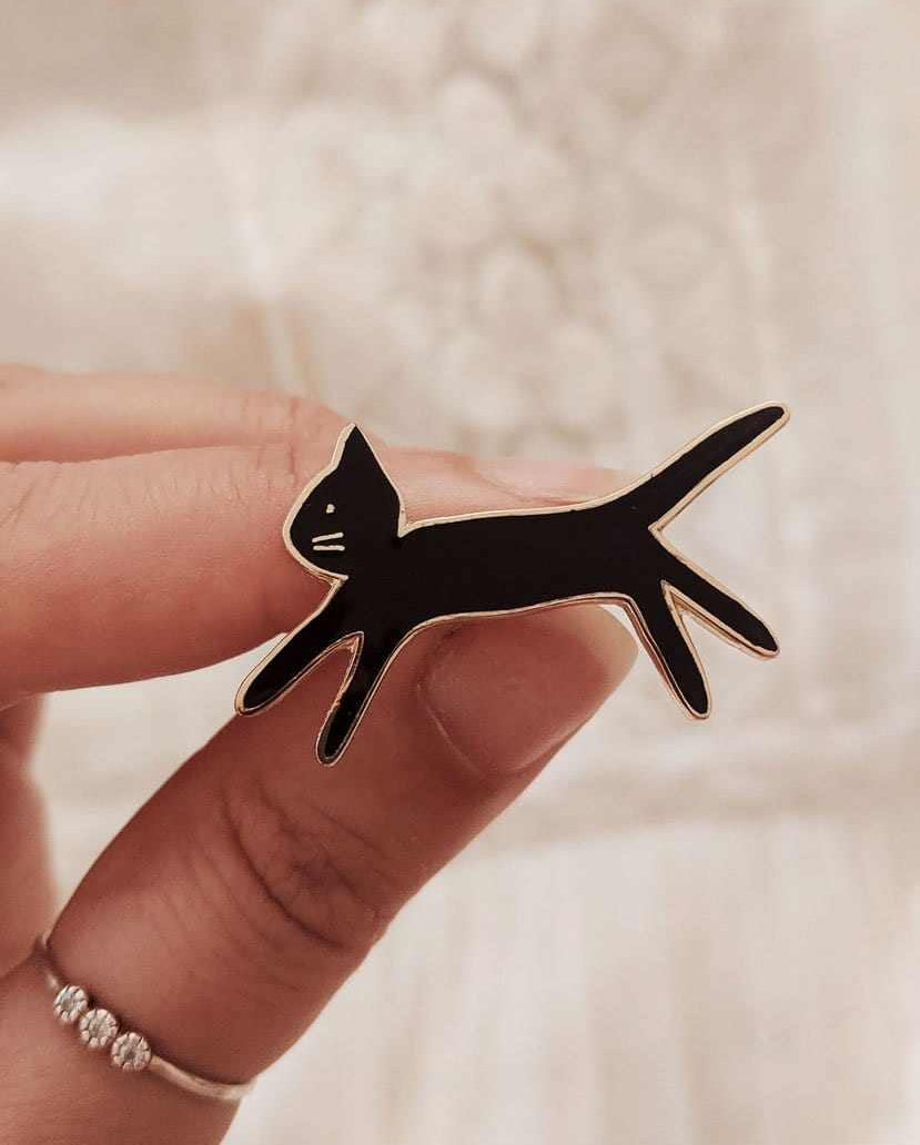 Hand holding black kitty enamel pin made of gold tone brass, 38mm size, designed in Montreal Canada